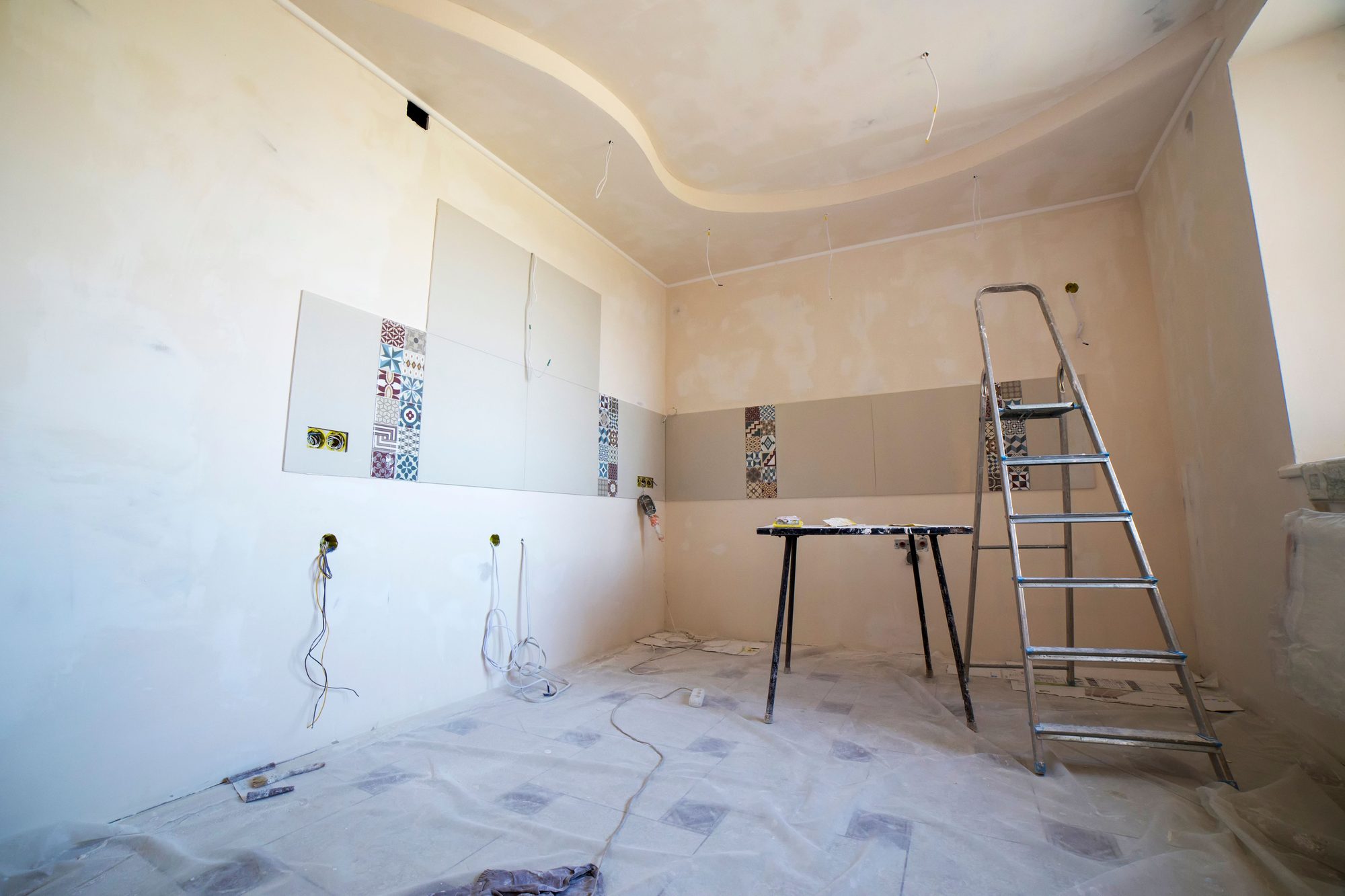 Bright room mid-renovation with fresh plaster walls, a decorative tile accent strip, a curved ceiling detail, and a ladder and work table set up for finishing work